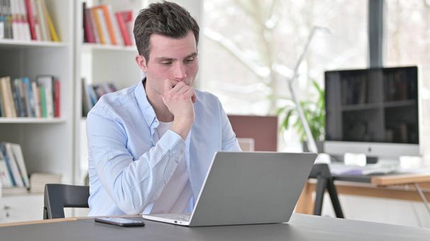 Hombre joven pensando y trabajando en el ordenador portátil
 - Foto, imagen
