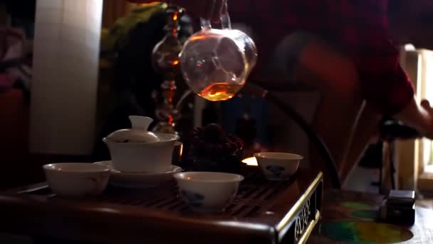 Ceremonia del té chino. Primer plano de la mano tomar la tetera y verter el té caliente en el frasco de servir de vidrio con taza de té de cerámica puesta en la mesa
. - Metraje, vídeo