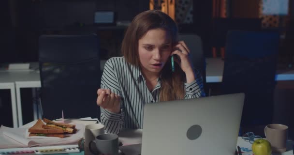 Woman office manager working with laptop and talking on smartphone with sad face. Young woman hearing bad news during phone conversation and looking disapointed. Concept of overwork. - Felvétel, videó
