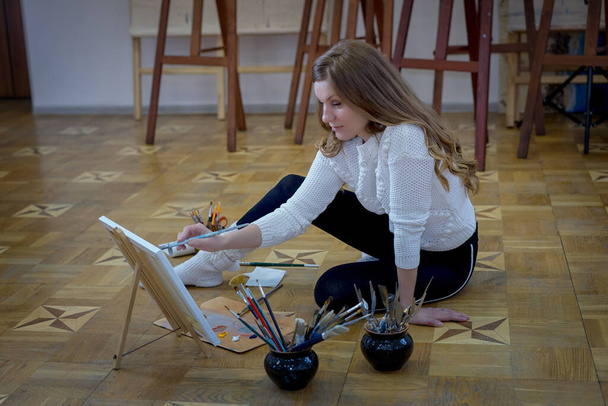 nő művész ül a padlón a művészeti stúdióban, és fest egy képet - Fotó, kép