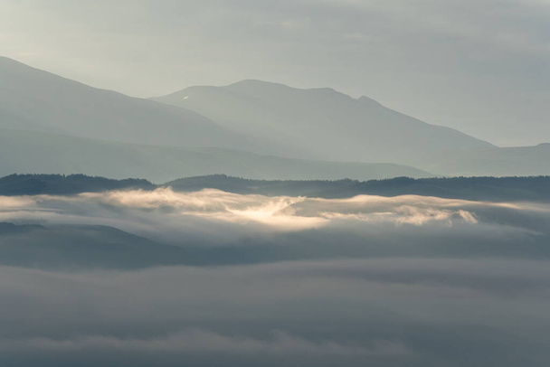 σύννεφα και ακτίνες της αυγής στην κοιλάδα του βουνού, απαλό φως νωρίς το πρωί, διαλογισμός στη φύση. Ευγενικοί λόφοι σε γαλαζωπή ομίχλη, σιλουέτες βουνών - Φωτογραφία, εικόνα