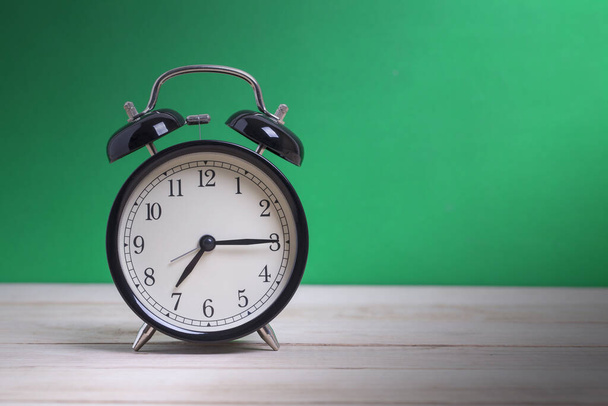 Un reloj despertador negro retro en tablero de madera con fondo verde
 - Foto, imagen