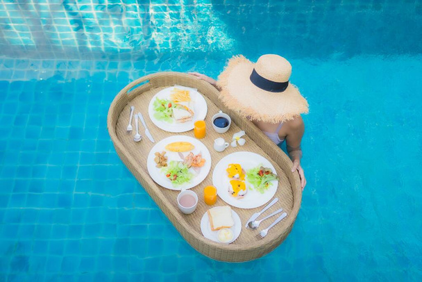 Retrato joven mujer asiática feliz sonrisa disfrutar con bandeja de desayuno flotante en la piscina en el complejo hotelero - Foto, imagen