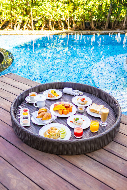 Flotaing breakfast tray around outdoor swimming pool with bread fruit egg coffee cup and juice - Photo, Image