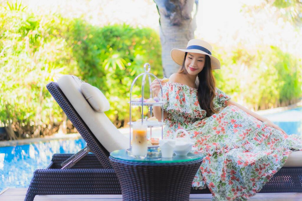 Schöne Porträt junge asiatische Frau mit Afternoon Tea Set mit Kaffee sitzen auf Stuhl rund um den Pool im Hotel Resort - Foto, Bild