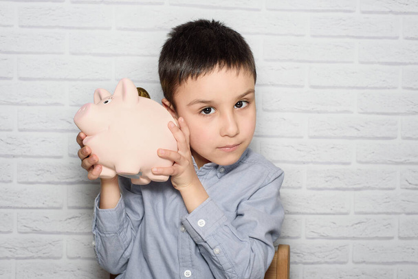 boy with pig piggy bank. childhood, money, investment and happy people concept. Child inserts coin into piggy bank - Foto, afbeelding