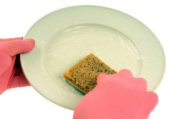 Egy tányér mosása közelről latex kesztyűvel és kétoldalas szivaccsal fehér alapon  - Fotó, kép