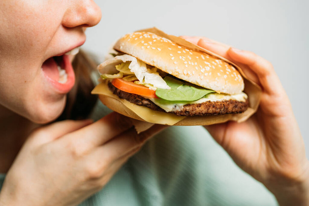 The girl holds a hamburger with her hands and eats it with appetite. Close up. - Foto, Imagen