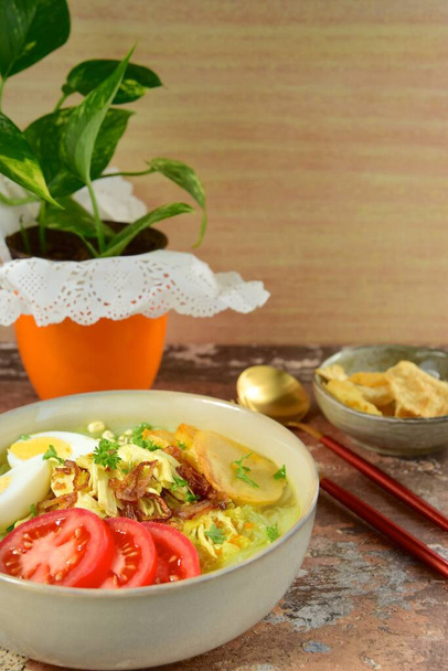 Soto Ayam, yellow turmeric chicken soup with vermicelli noodles, shredded chicken, boiled egg, fried potato, sprouts, tomato, parsley and fried shallots, served with Emping. Popular Indonesian food - Photo, Image