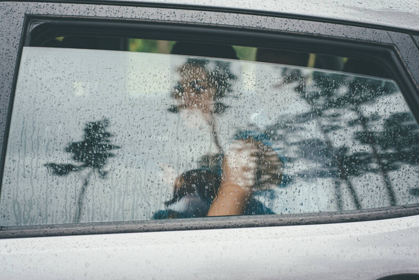 Gri araba camındaki yağmur damlalarının arasından görünen, gelin bir kızın zar zor görünen romantik çizgileri. - Fotoğraf, Görsel