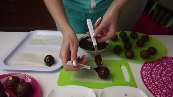 A woman lays on the surface balls of chocolate sponge cake. It sprinkles. Makes a Potato cake. Next to the plates are cake blanks, liquid chocolate and colored sprinkles. - Metraje, vídeo
