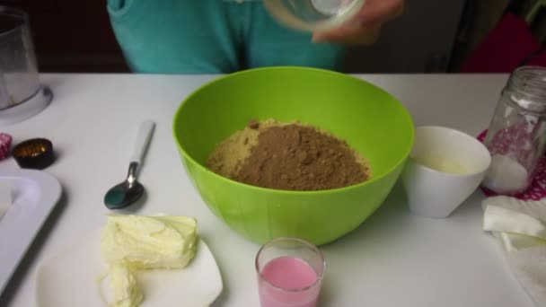 A woman adds cocoa and butter to crumbled cookies. Other ingredients for making Potato cookies are laid out nearby. - Metraje, vídeo