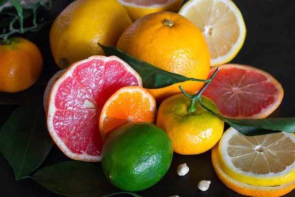 fresh citrus fruits orange, mandarin, lime, grapefruit, lemon and green leaves on a black background close-up - Foto, afbeelding