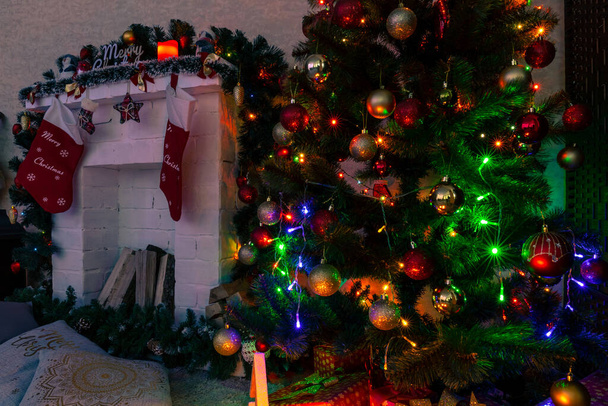 Noel ağacının yanında çoraplarla süslenmiş bir şömine, hediyeler, oyuncaklar ve çelenk ışıkları. - Fotoğraf, Görsel