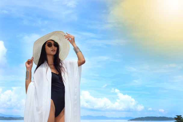 Mix Race Tanned Skin Woman en Big Hat noir Lunettes de soleil maillot de bain prendre des vacances en été Ocean Island scène sur ciel tropical bleu et nuage, espace de copie pour le logo texte
 - Photo, image