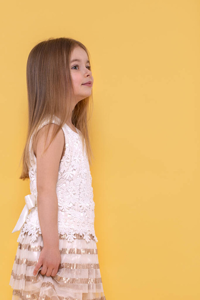 Halblanges Profil-Porträt eines kleinen träumenden Mädchens mit langen blonden Haaren vor gelbem Hintergrund mit Kopierraum im Studio - Foto, Bild