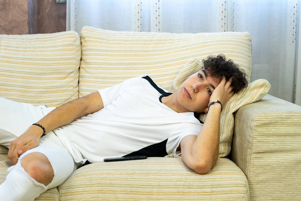 Hombre joven posando en un sofá blanco en su sala de estar
 - Foto, Imagen