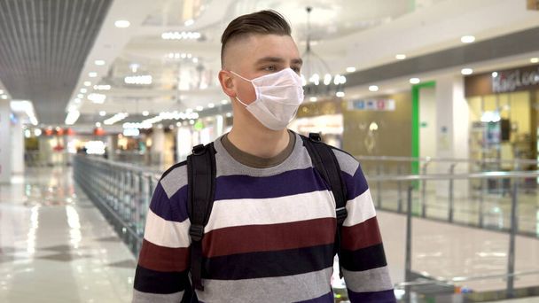 Ένας νεαρός με ιατρική μάσκα μπαίνει σε ένα εμπορικό κέντρο. Ο μασκοφόρος προστατεύει τον εαυτό του από την επιδημία του κινεζικού ιού "2019-nkov" - Φωτογραφία, εικόνα