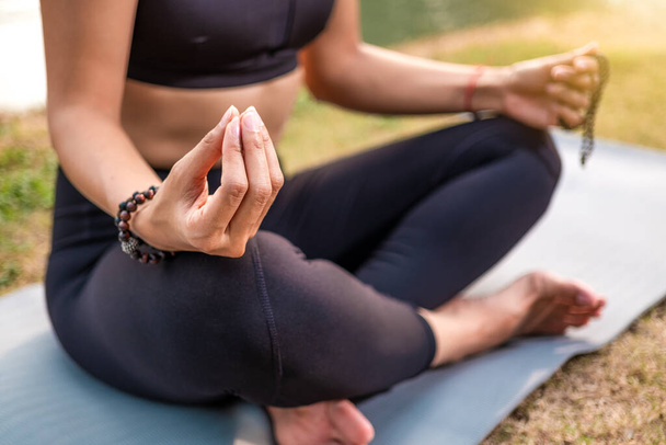 Mujer sentada en postura de yoga de buda. Primer plano en la mano sosteniendo cuentas asiáticas o collar con perlas
 - Foto, Imagen