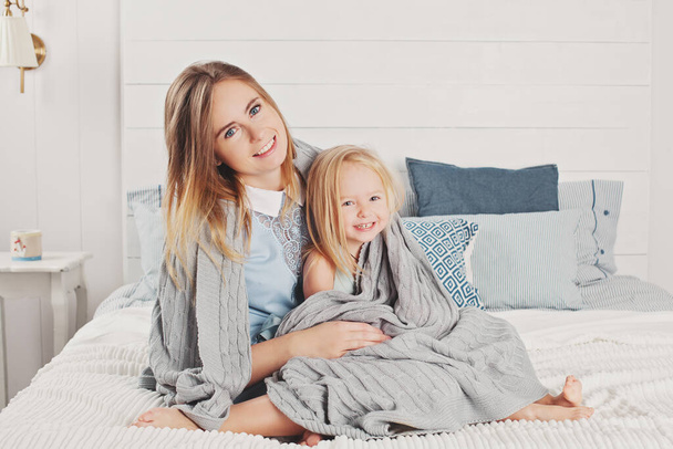 Щаслива родина вдома. Приваблива мати і маленька дочка сидять на ліжку
 - Фото, зображення