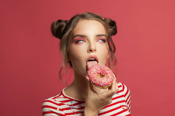 Funny woman eating donut and enjoying on pink background - Фото, изображение