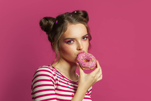 Perfektní model žena jíst podrážděné koblihy na barevném růžovém pozadí - Fotografie, Obrázek