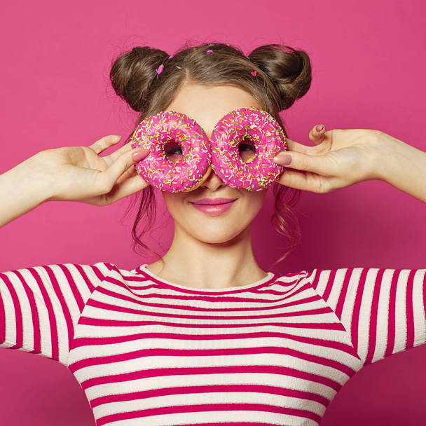 Çekici bir genç kadın pembe arka planda iki donut gösteriyor. - Fotoğraf, Görsel