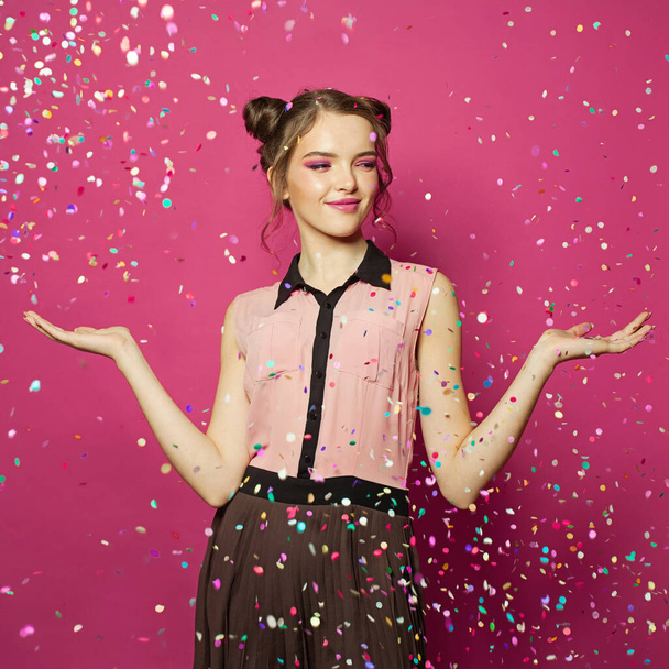 Portrait of beautiful young model woman in falling colorful confetti on bright pink background - Photo, Image