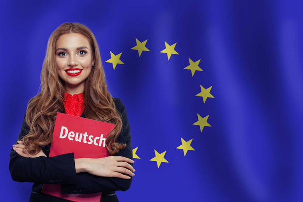 Mujer feliz estudiante con libro Deutsch en el contexto de la bandera de la Unión Europea. Libro con inscripción Deutsch sobre el idioma Deutsch
 - Foto, Imagen