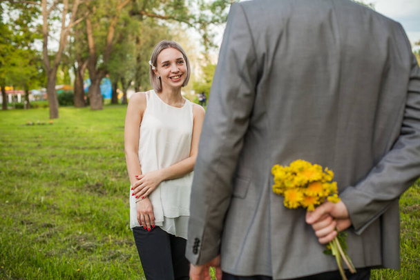 Gelukkig meisje en jonge man met bloemen in de hand. Romantische verrassing en dating concept - Foto, afbeelding