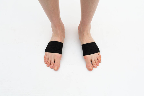 cuff-tie for the anterior part of the foot with a metatarsal roller on the legs of a woman to correct the big toe for hallux valgus, 2 legs, isolated close-up, white background - Фото, изображение