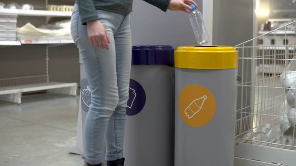 A young woman throws a plastic bottle into the trash. Special containers for sorting garbage. Container for plastic. - Photo, Image