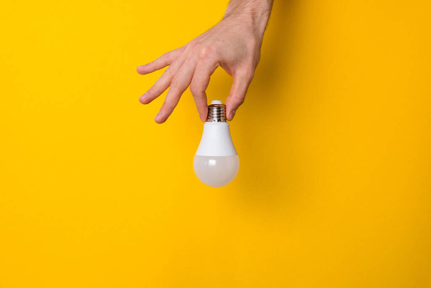 closeup hand holding white led lighting bulb against a yellow wide background banner with copyspace. concept of idea, energy and ecology - Valokuva, kuva