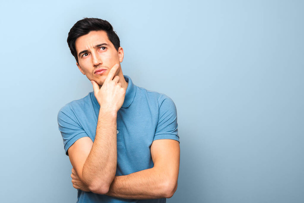 what can I do. pensive man in blue polo shirt against a blue background with hand on his chin and looking up with copy space. - Photo, Image