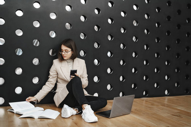 Education, student lifestyle and career concept. Portrait of young smart girl working on project, sit co-working space or college lounge on floor, reading book and type report in laptop - Foto, Imagem