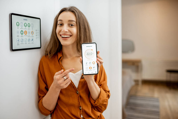 Happy woman controlling smart home with a touch screen devices - Fotó, kép