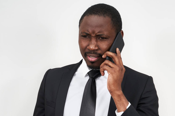 Szoros kép a dühös fiatal afrikai férfi sikoltozik, miközben beszél okostelefonon keresztül szürke háttér - Fotó, kép