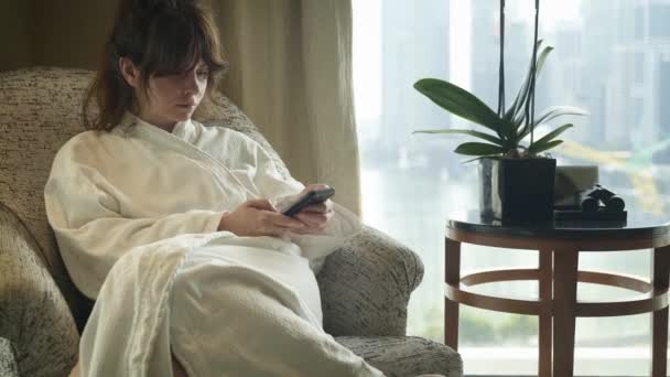 Una donna che naviga in internet utilizzando lo smartphone nel sofisticato hotel di fronte alla finestra panoramica. Singapore skyline sullo sfondo. colpo in tempo reale
. - Filmati, video