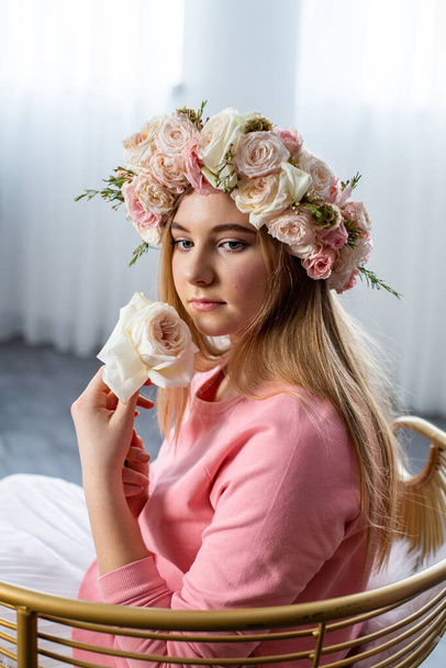νεαρή όμορφη ξανθιά κάθεται χαμένη στη σκέψη με ένα λουλούδι στο χέρι της - Φωτογραφία, εικόνα