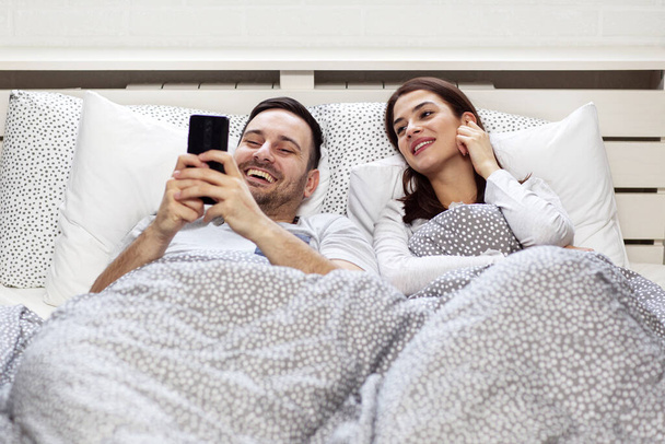 Couple with mobile phone in bed in the morning - 写真・画像