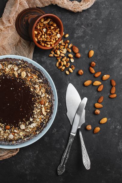 Chocolate cake, chocolate cake, dessert with nuts. Roasted peanuts, almonds and hazelnuts. On dark background. The view from the top. The view from the side. Space for text. - Photo, image