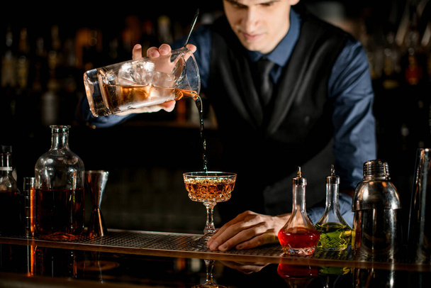 Young bartender pours a ready-made cold cocktail into wineglass. - Fotografie, Obrázek