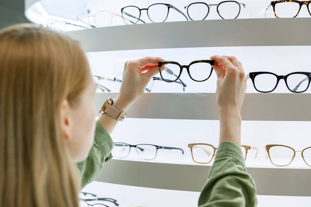woman pick a eyeglasses from shelf in optics store - Photo, Image