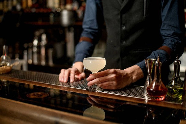 bartender in blue shirt holding white cocktail in glass on the bar - Valokuva, kuva