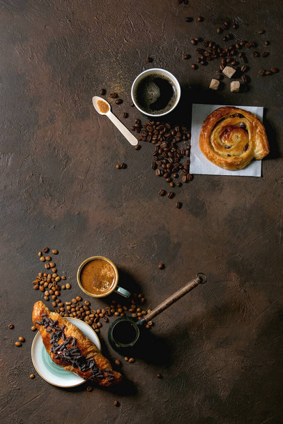 様々な伝統的なフランスのパイ生地のレーズンとチョコレートパン、コーヒーとミルクの様々なカップとクロワッサン、セブ、濃い質感の背景に砂糖のリサイクル木製のスプーン。平面、空間 - 写真・画像