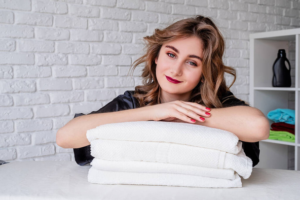 sorridente giovane donna su un mucchio di asciugamani su sfondo mattoni bianchi
 - Foto, immagini