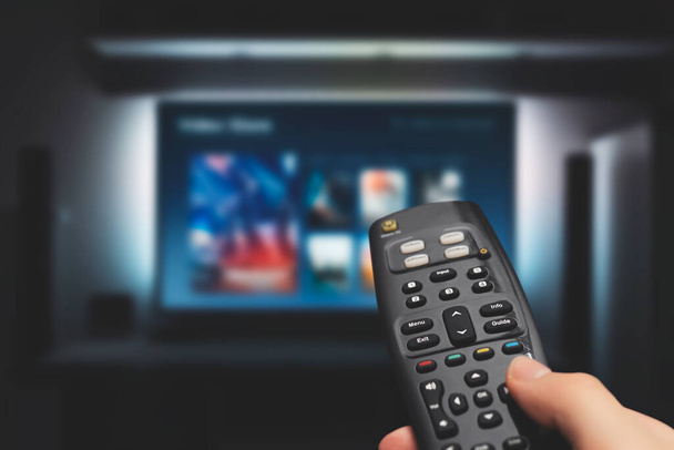 VOD service on television. Man watching TV, streaming service, video on demand, remote control in hand. - Photo, image