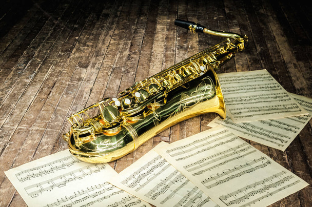 lesklý zlatý saxofon leží v blízkosti listů hudebních písmen na dřevěném jevišti - Fotografie, Obrázek