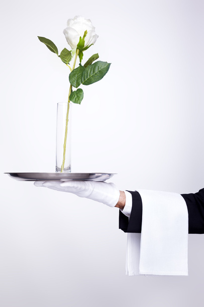 Waiter holding silver tray with a glass jar and flower over gray - Zdjęcie, obraz