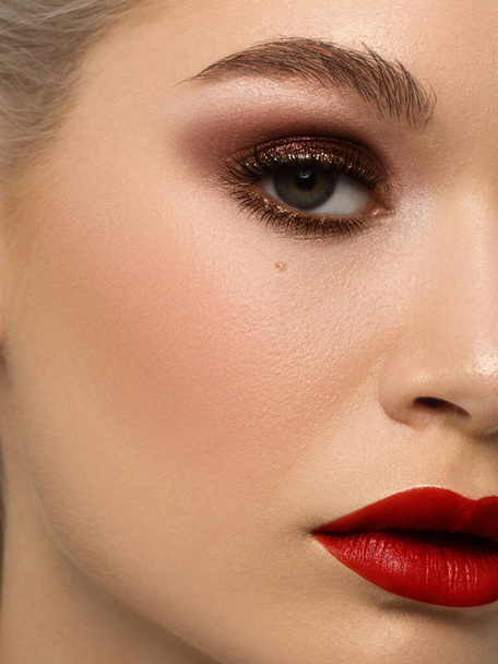 Half a beauty portrait with beautiful fashionable evening make-up, black smoky eyes and extremely long eyelashes. Red lipstick on the lips. Cosmetology and spa facial skin care - Фото, изображение